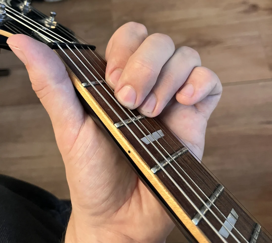 A left hand holding a A chord on a guitar neck, seen from the player's viewpoint with the nut visible for reference
