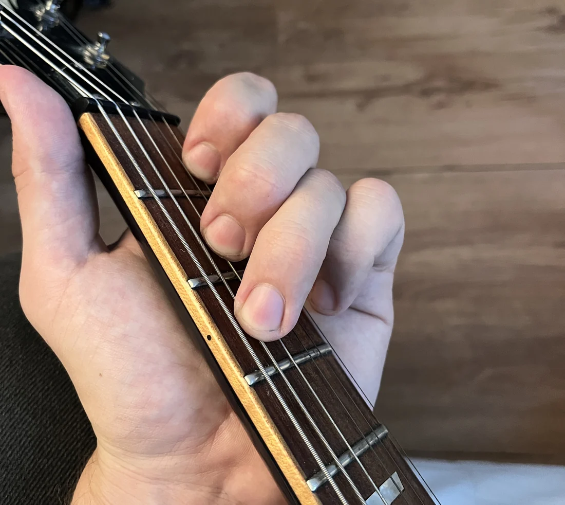 A left hand holding a C chord on a guitar neck, seen from the player's viewpoint
