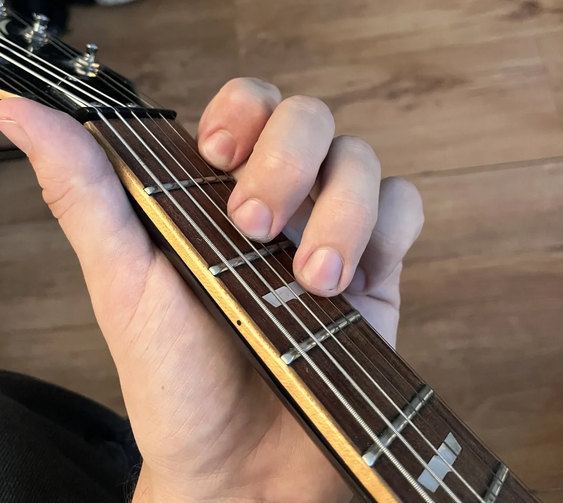 A left hand holding a Dm chord on a guitar neck, seen from the player's viewpoint with the nut visible for reference