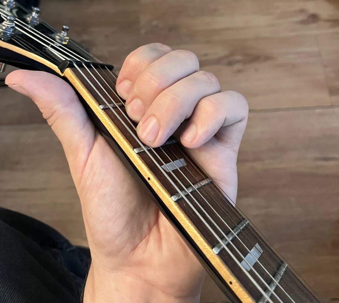 A left hand holding a E chord on a guitar neck, seen from the player's viewpoint with the nut visible for reference