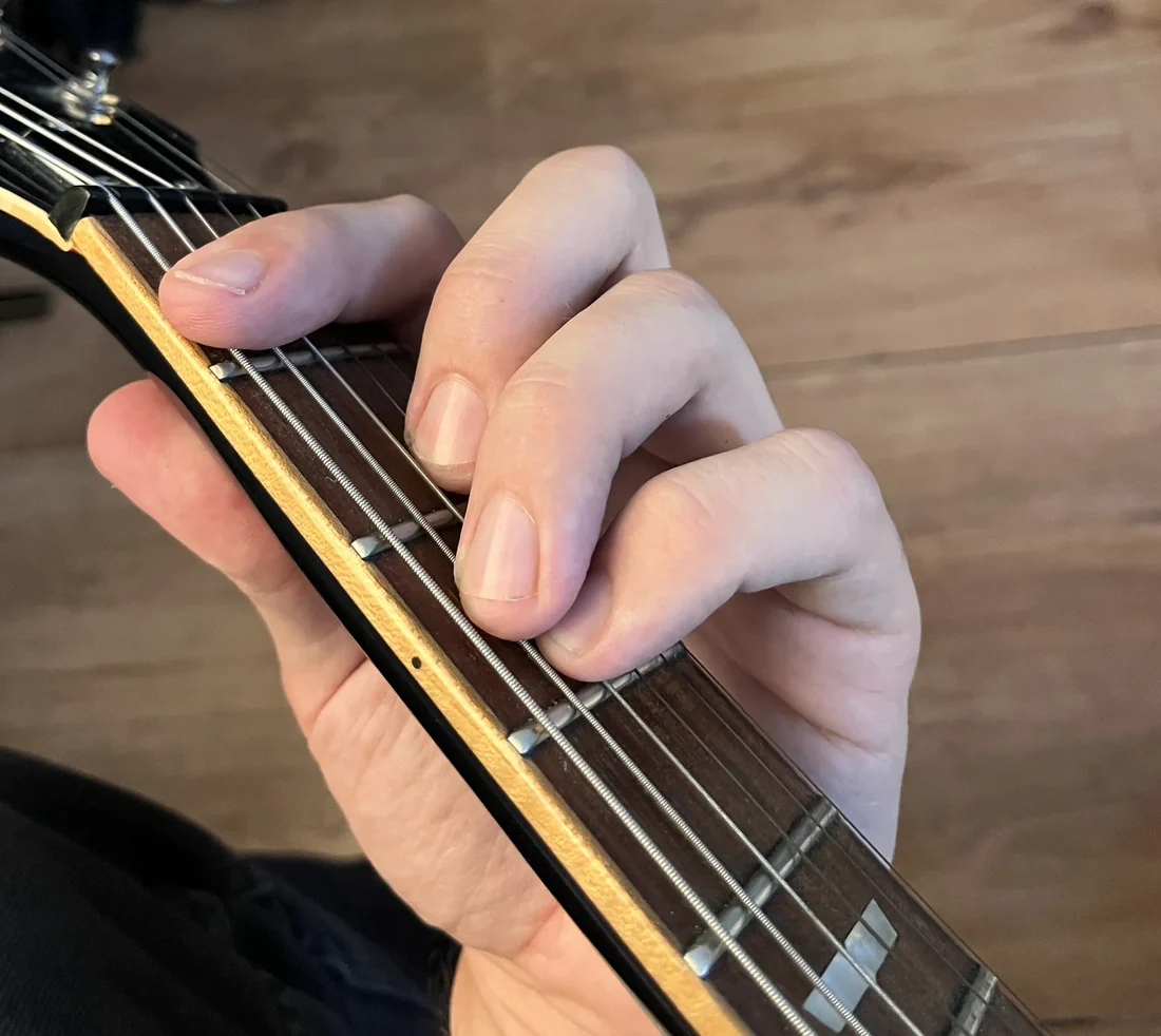 A left hand holding a F chord on a guitar neck, seen from the player's viewpoint with the nut visible for reference